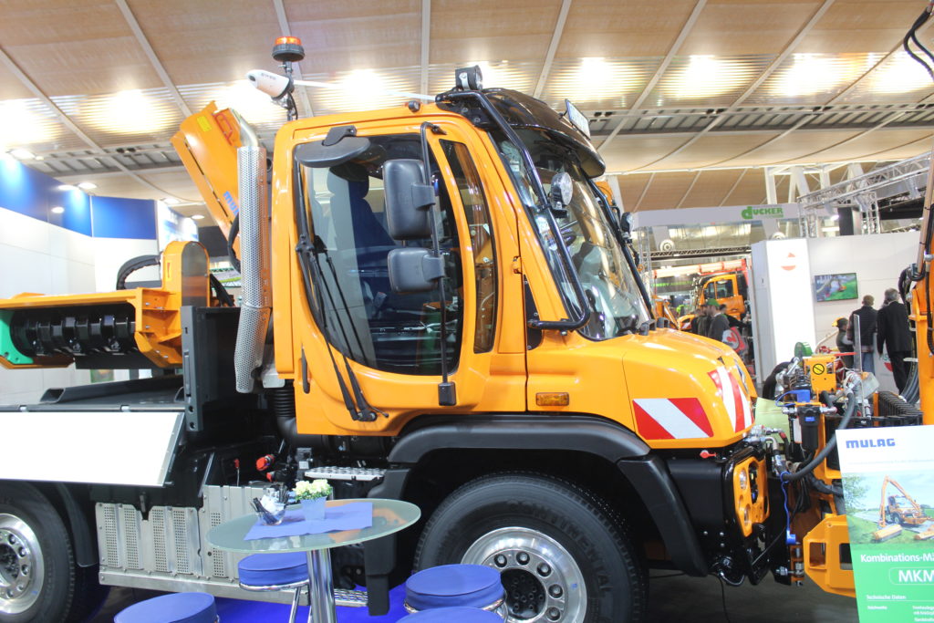 Nosič Mercedes-Benz UnImog U 430 s otočným sedadlem spolujezdce, panoramatickými dveřmi a posuvným řízením. Za kabinou je patrné rameno s mulčovací hlavou Mulag BRK 1200.