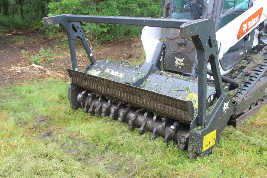 Detail lesní frézy Bobcat se spirálovým rotorem a hydraulicky ovládanou horní klapkou.