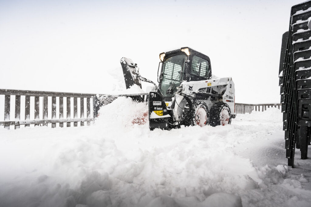 Smykem řízený nakladač Bobcat při práci s hydraulicky poháněnou sněhovou frézou.